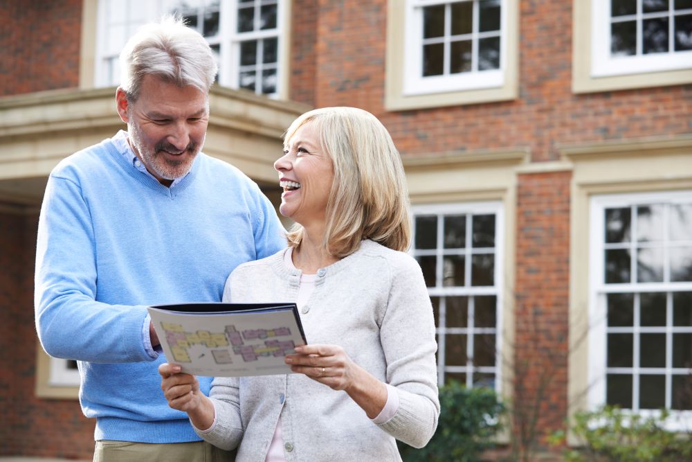 Smiling couple reviewing a floor plan outside their home, representing satisfied clients of residential moving services.
